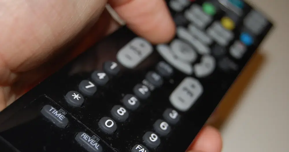 Mão segurando controle remoto de televisão com botões numéricos